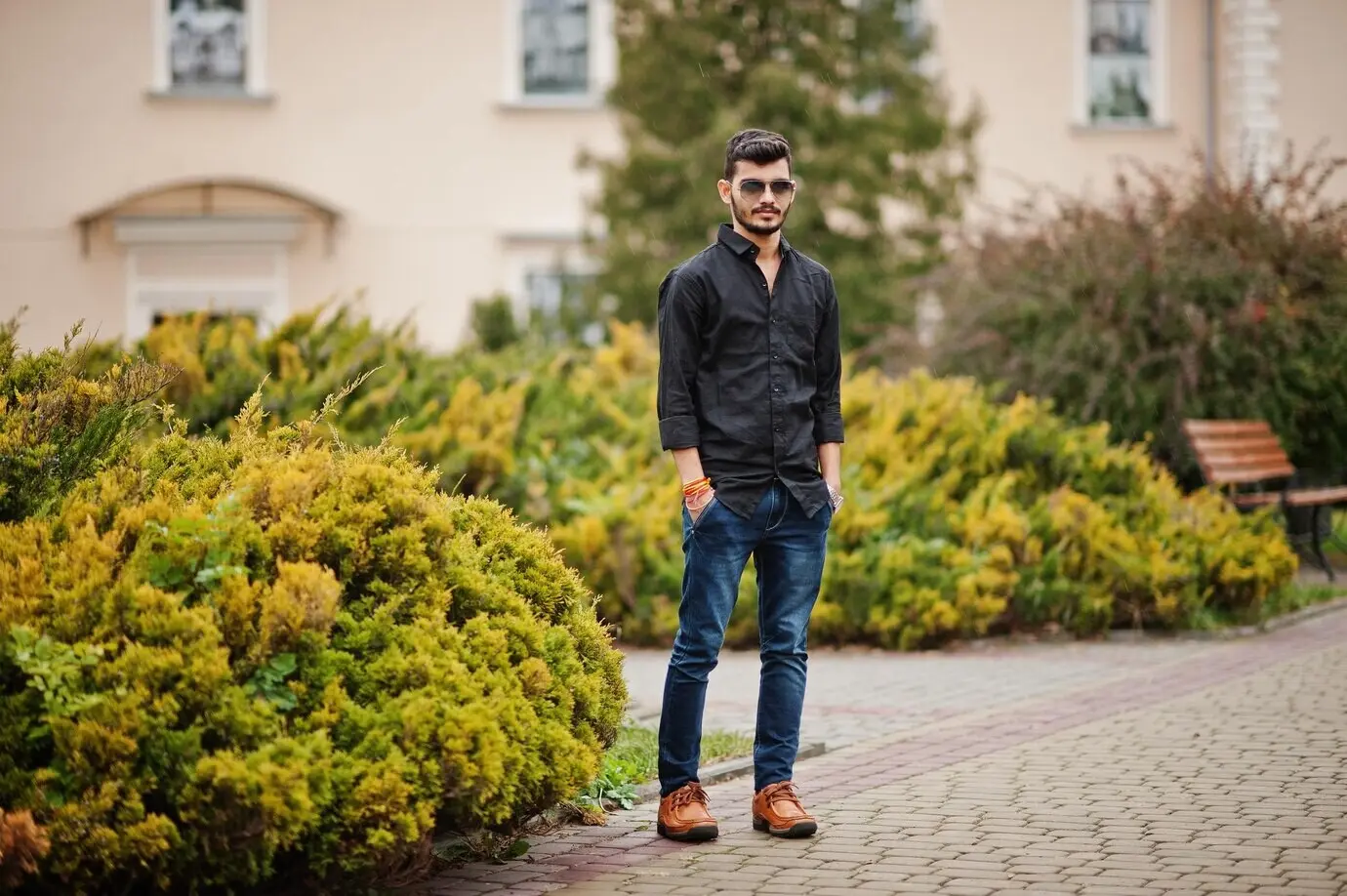 A stylish Indian man in a black shirt and sunglasses posed outdoors.